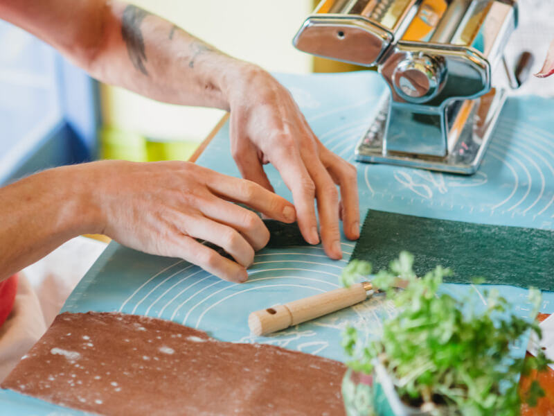 A close up of a person making green coloured fresh pasta by hand