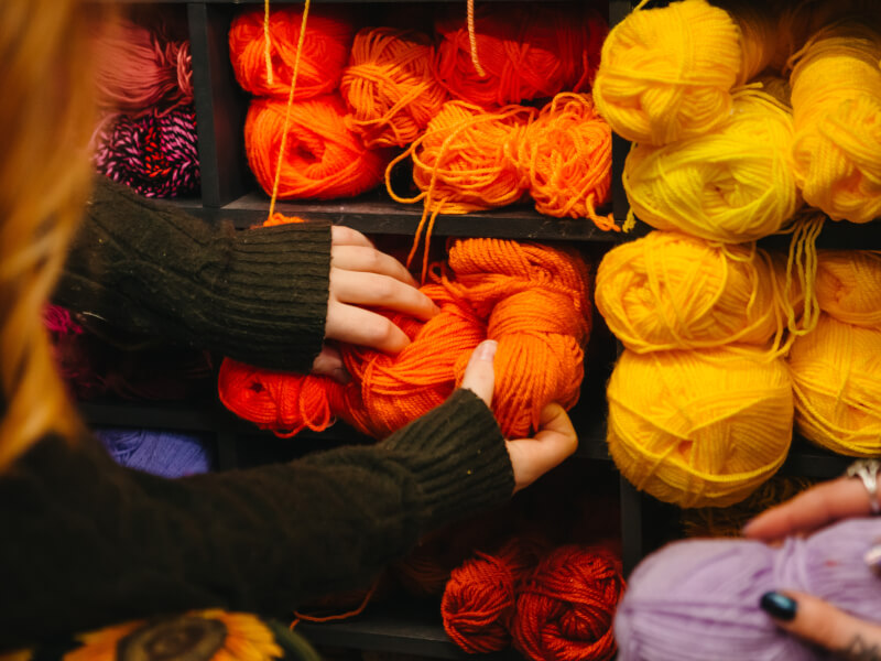 Hands picking out yarn from a cupboard filled with colourful yarn.