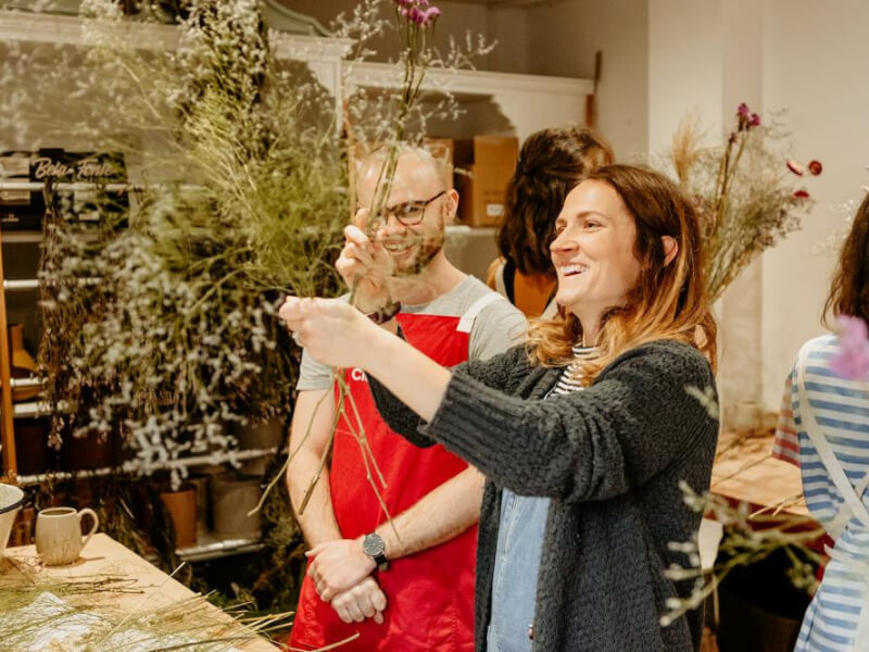 A man and a woman smiling while admiring the dried flower bouquet she's made