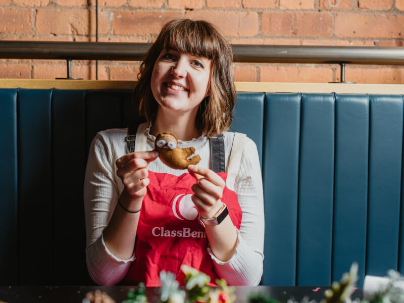 Woman wearing apron holding a felt sewn sloth.