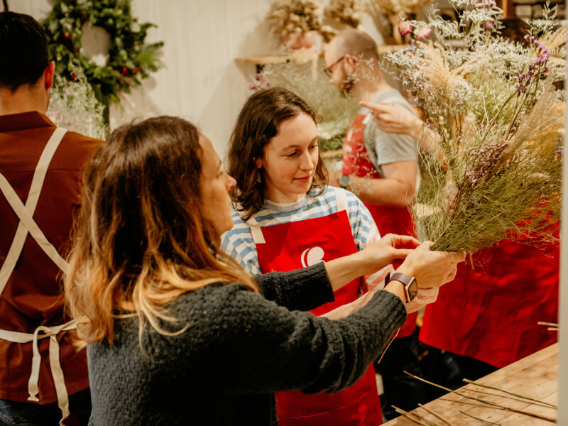 A woman is showing another woman how to make a bouquet from dried flowers