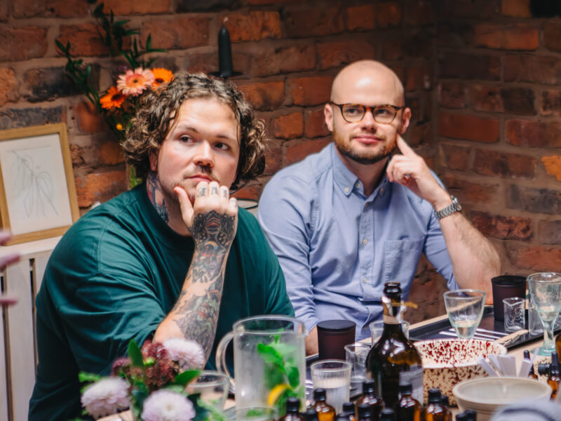 Two men listening to their teacher at a craft workshop