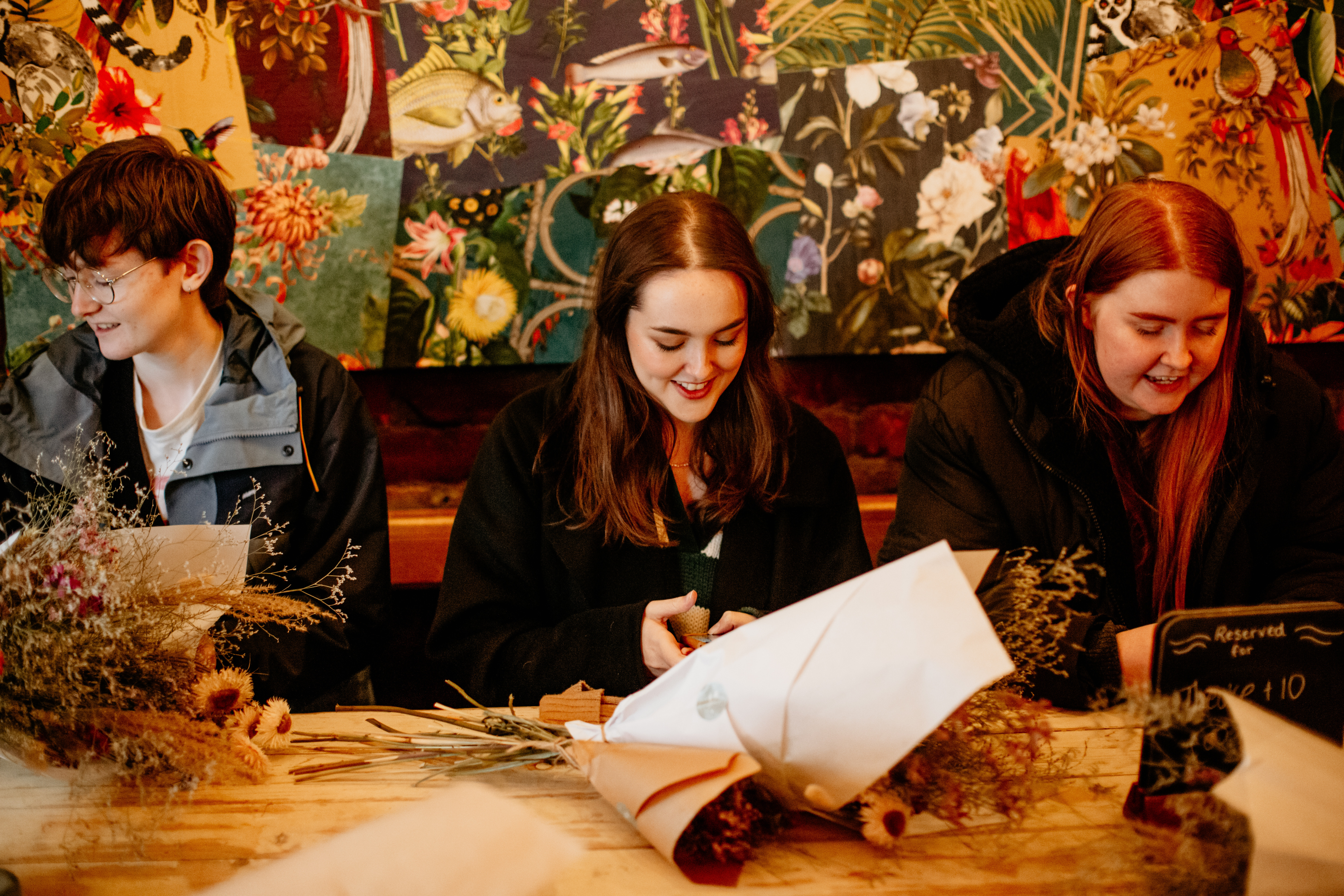 Three people smiling and talking as they arrange flowers together