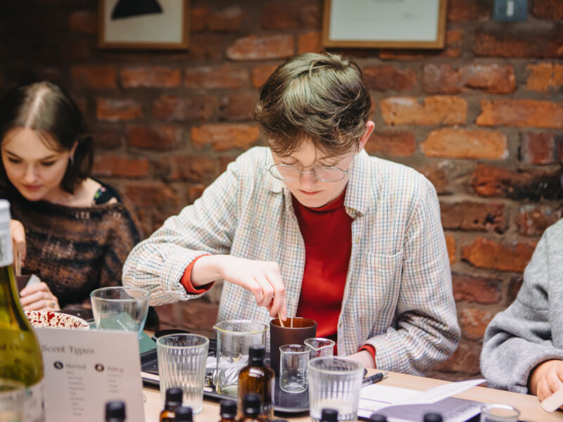 A person is making a handmade candle in an amber glass jar