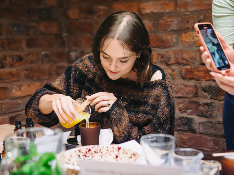 A woman is pouring melted wax into a candle container 