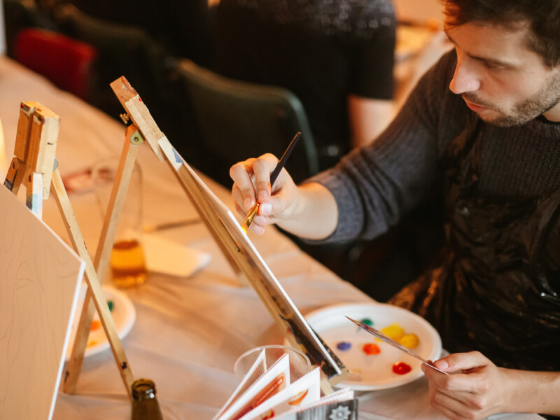 A man paints a canvas at a paint and sip class.