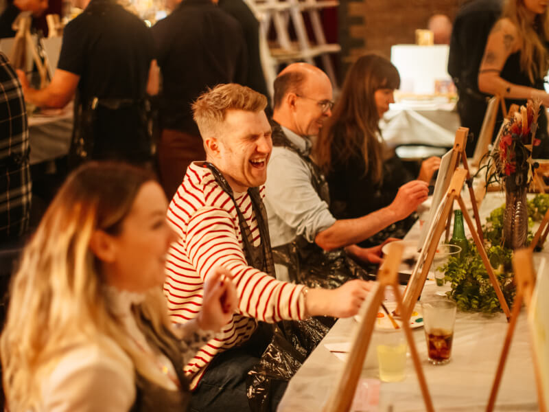 A group of people painting and laughing at an art class