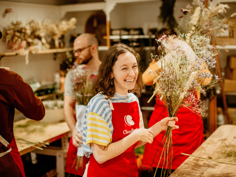 Woman wearing apron smiling holding handmade dried flower bouquet.