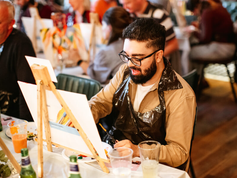 A man with a beard painting on a canvas at a painting workshop