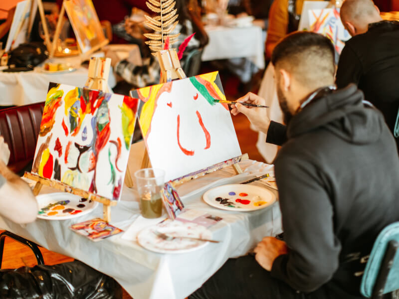 A group of people sitting at a table, each painting on an easel