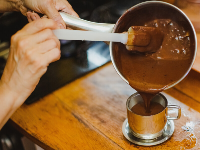 Person pouring melted chocolate from a sauce pan into a cup.