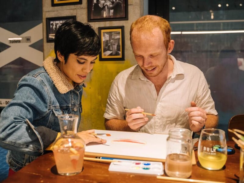 A man and a woman smiling while sharing a painted canvas