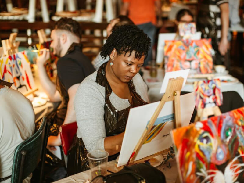 A woman concentrates as she paints on a canvas