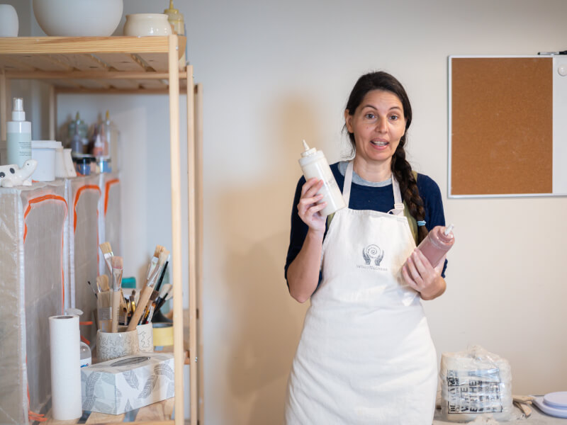 A woman holding paint bottles at a pottery painting class