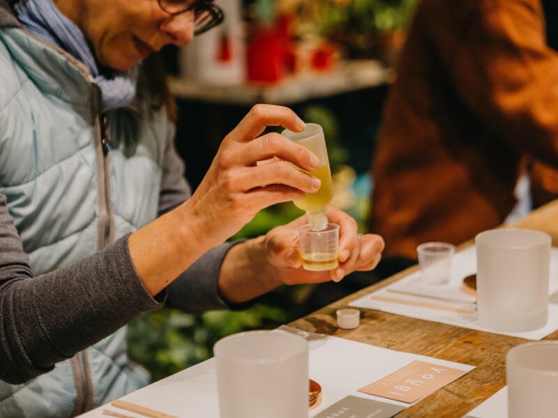 A woman wearing glasses decants essential oils into a small glass container