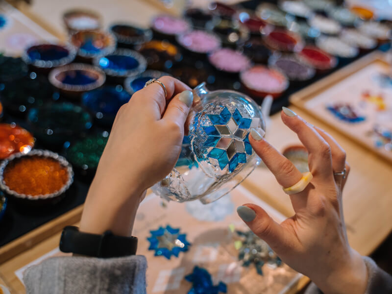hands sticking down pieces for their mosaic art on a glass bowl.