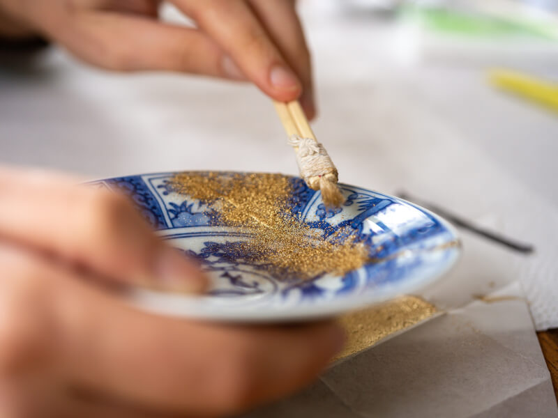 A person sprinkling gold powder in a kintusgi class.