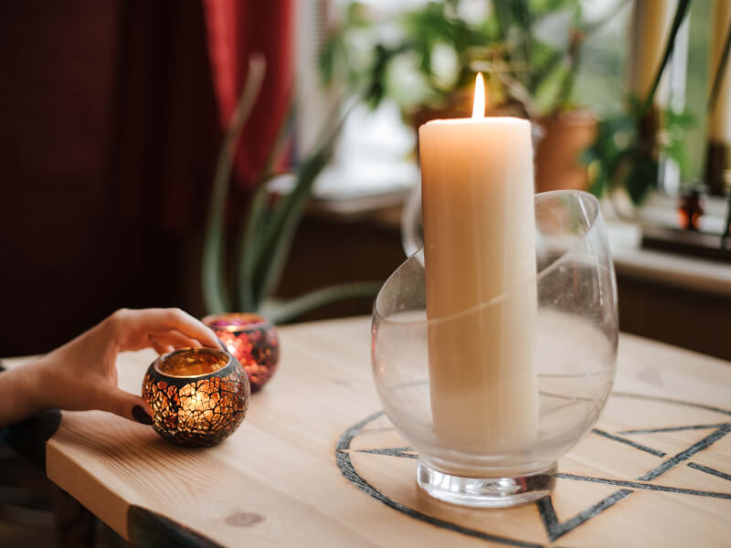 A lit candle in a glass jar and a person lighting other smaller candles
