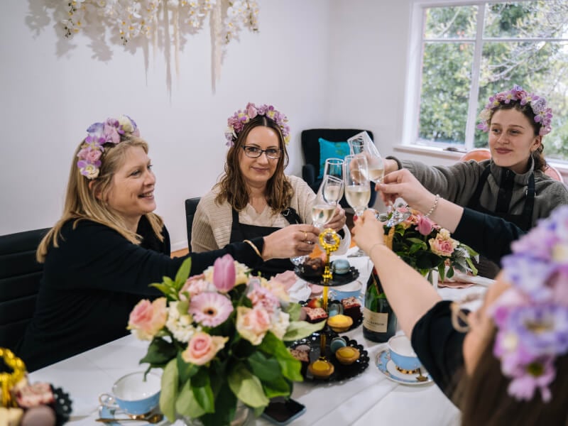A group of women at a hen party wearing flower crowns and toasting with sparkling wine