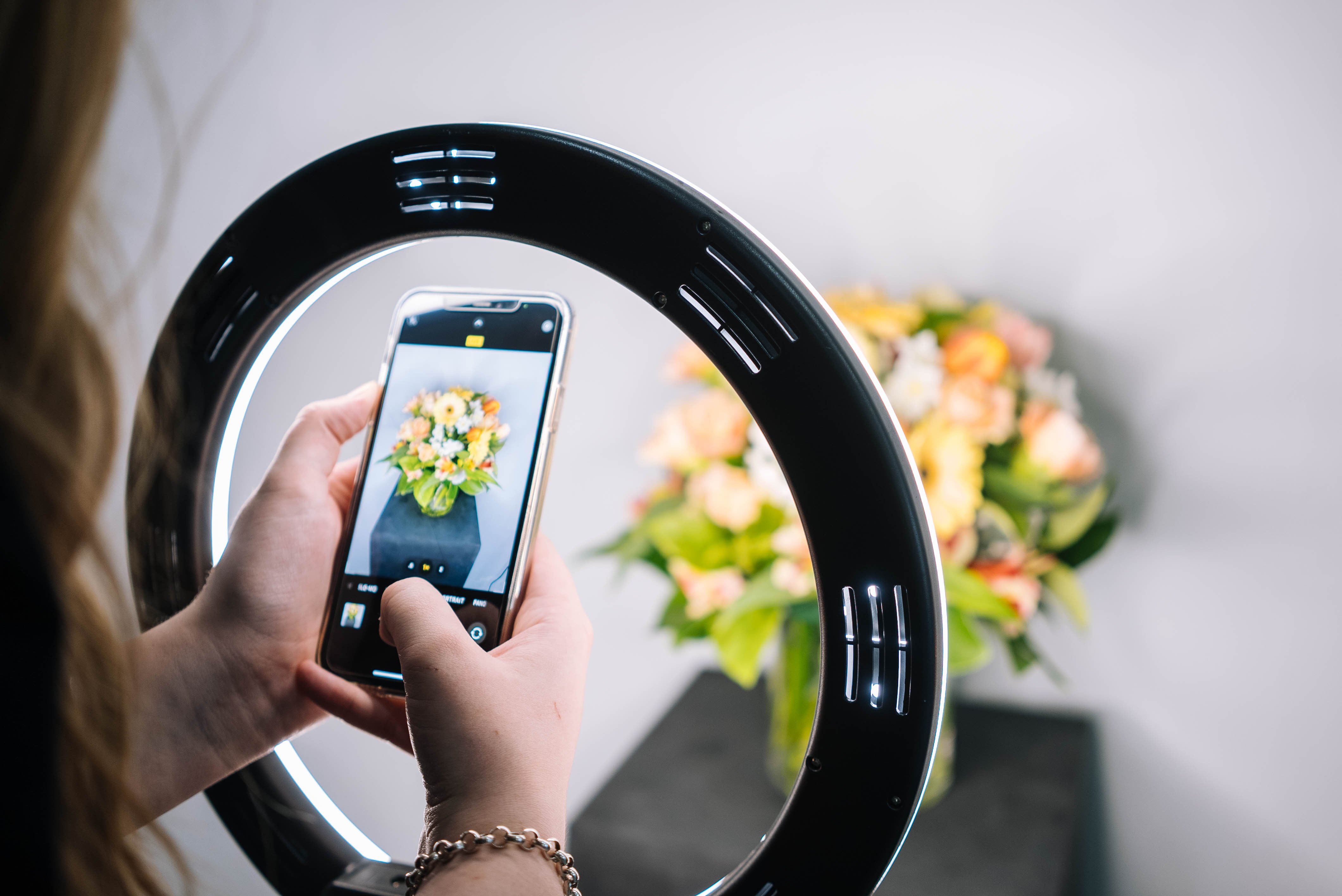 Person using a smartphone and ring light to take a picture of flowers