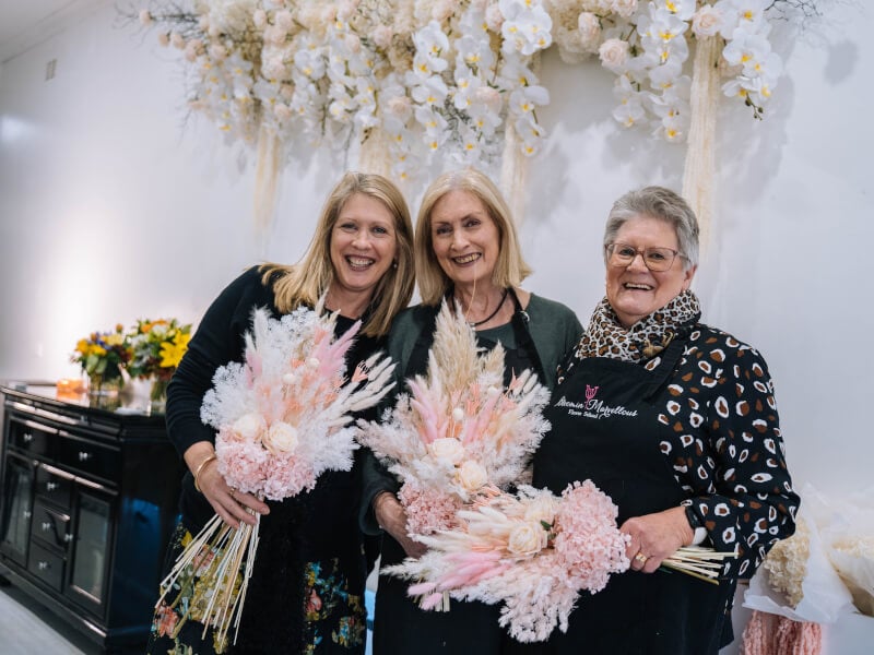 A group of smiling women holding flower bouquets.