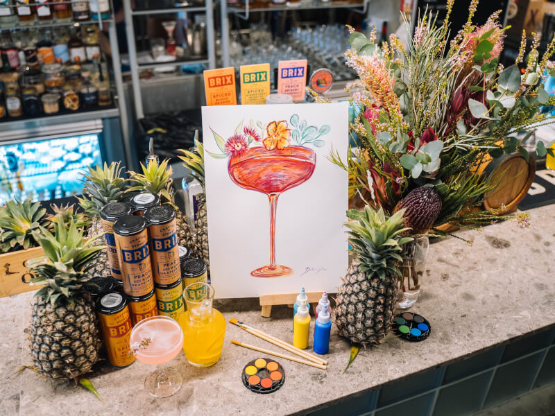 A canvas painting of a cocktail sat on a bar filled with cocktail ingredients.