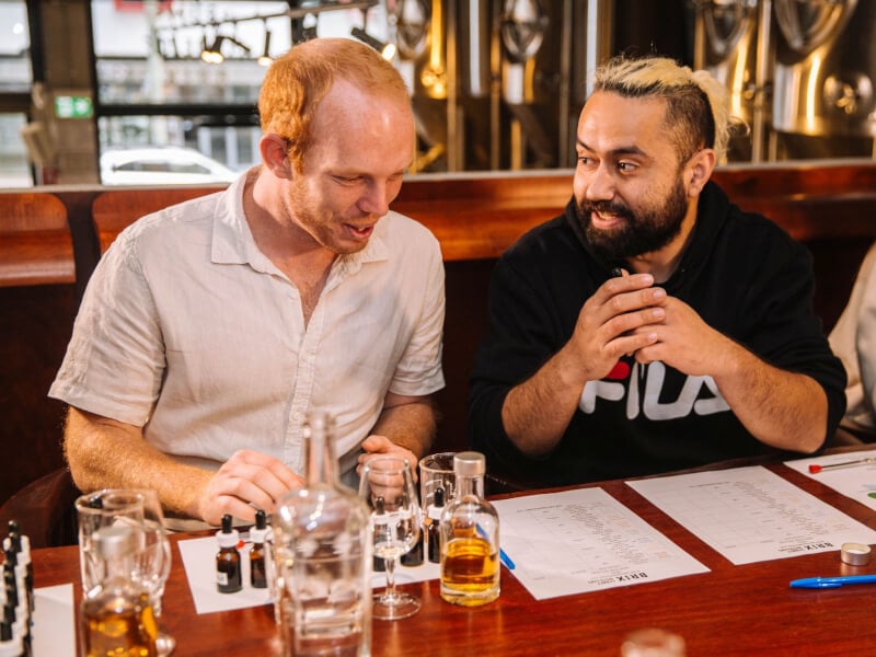Two men laughing together as they work at a cocktail class