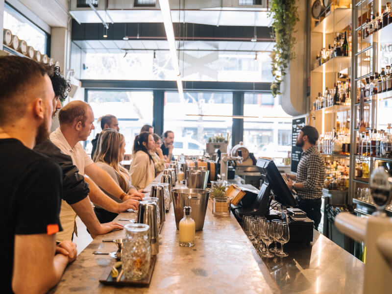 A row of people stand on one side of a cocktail bar at a cocktail class
