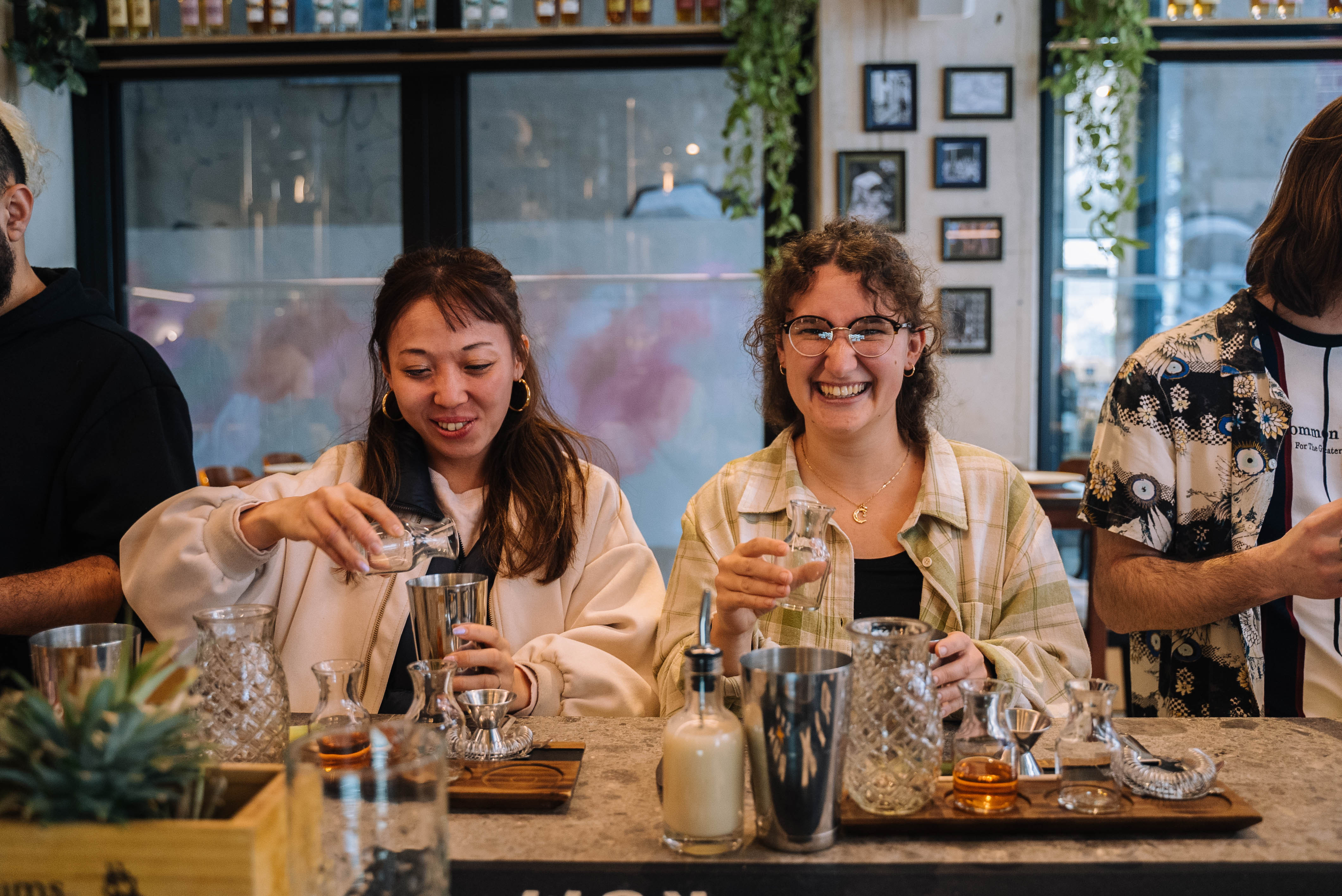 Two women smiling as they make cocktails side by side
