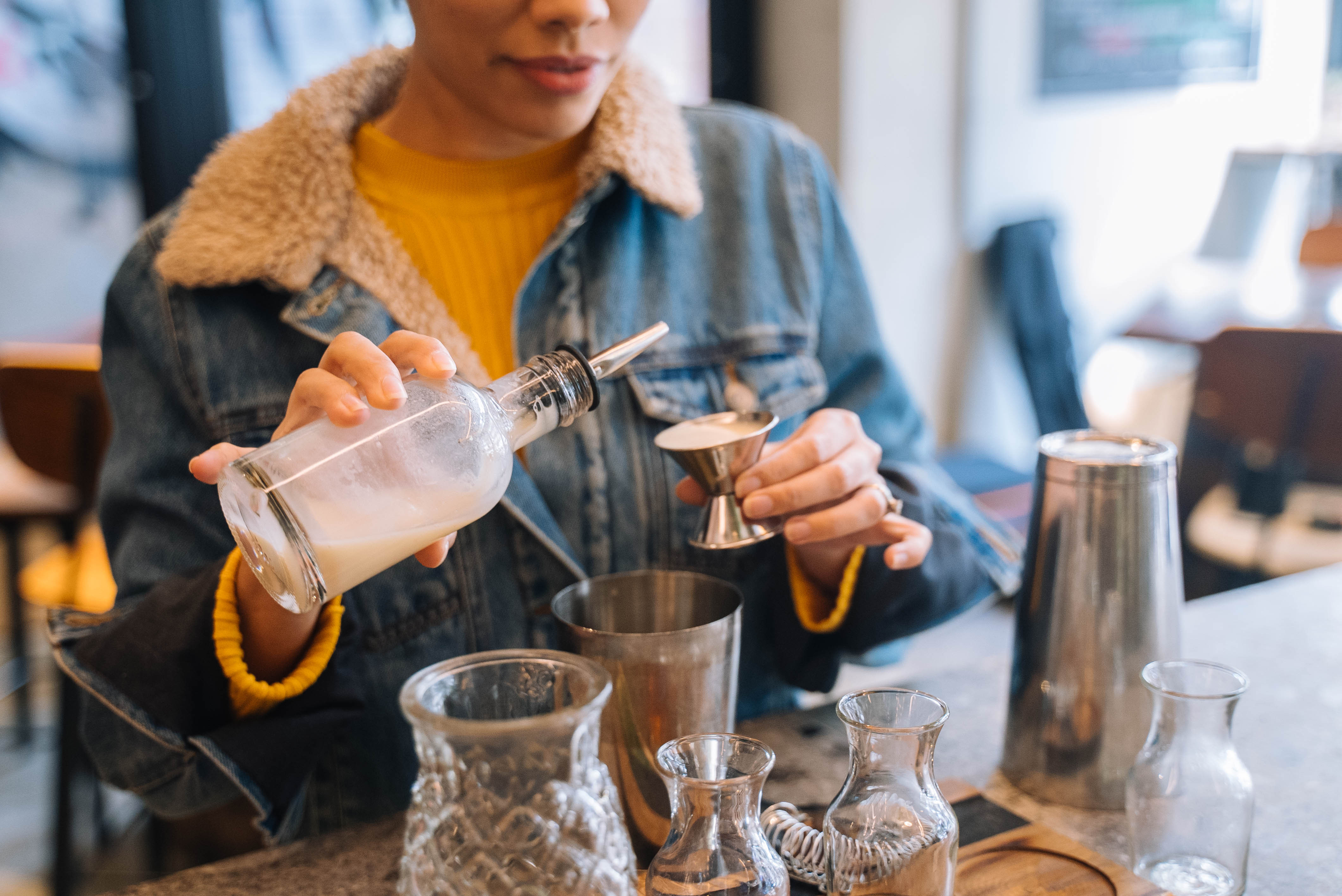 A person in a denim jacket pouring liqueur into a metal jigger