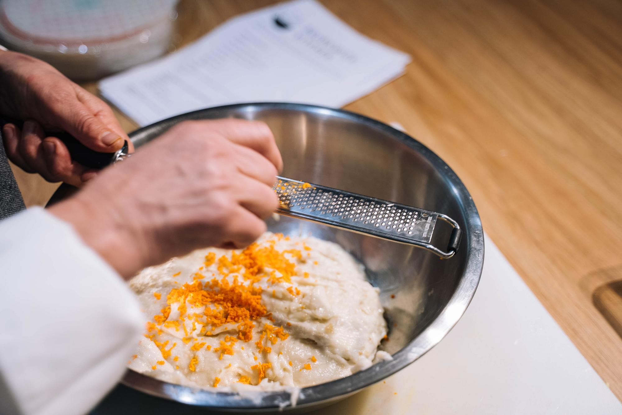 A person grating orange zest into a bowl of ingredients