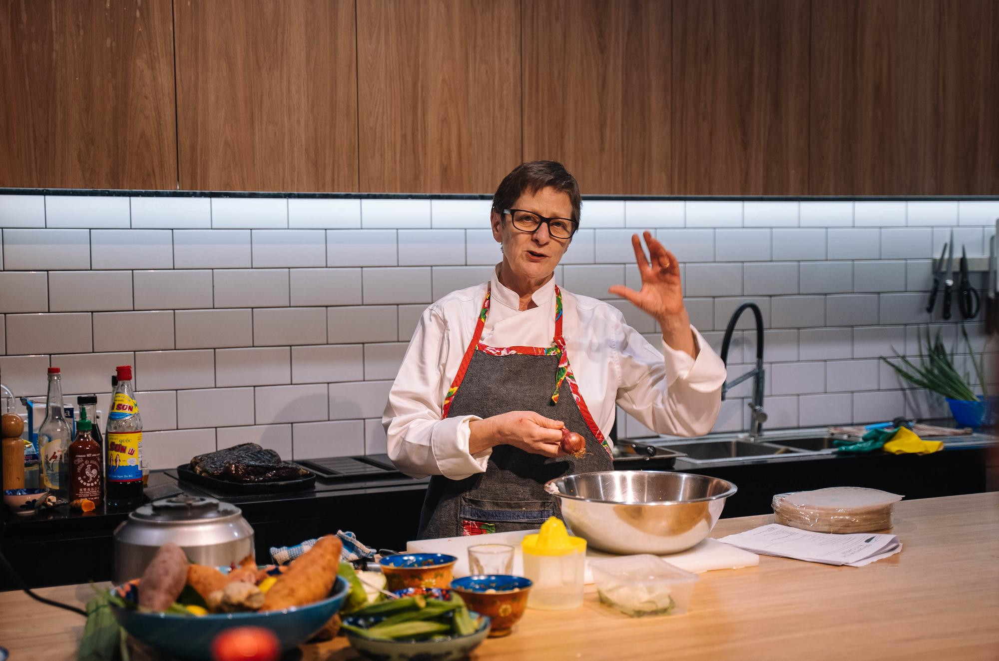 A person mid demonstration of a cooking class in a kitchen full of ingredients.