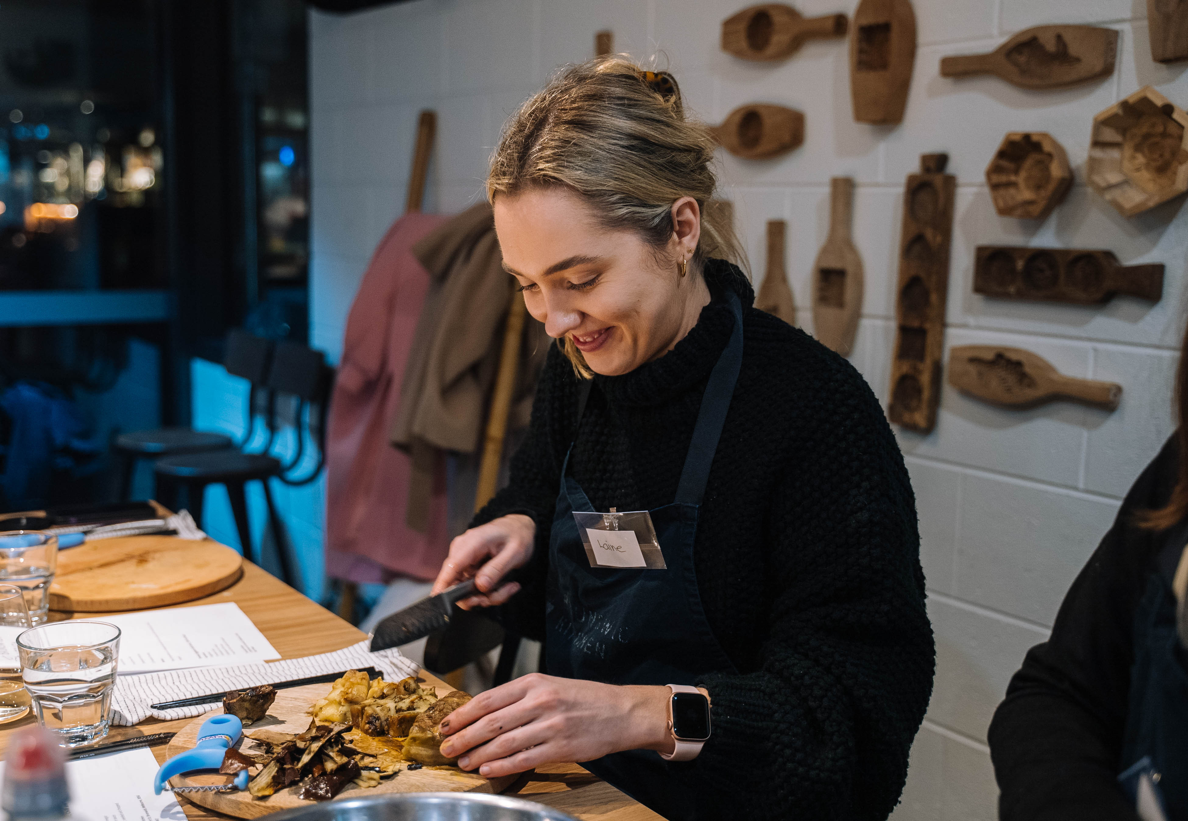 A smiling woman cuts food at a cooking class.