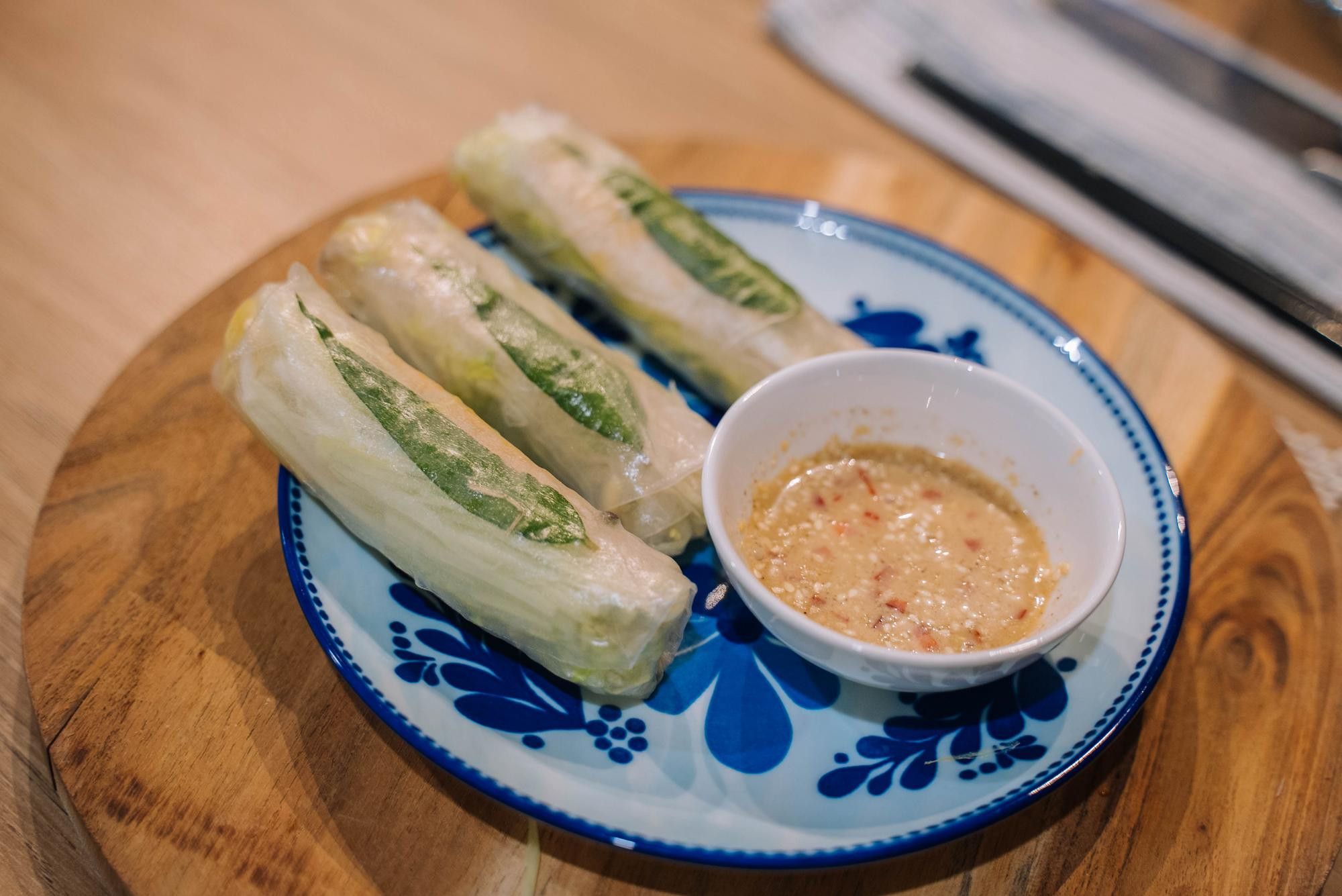 Three vegetable spring rolls on a plate with a bowl of dipping sauce