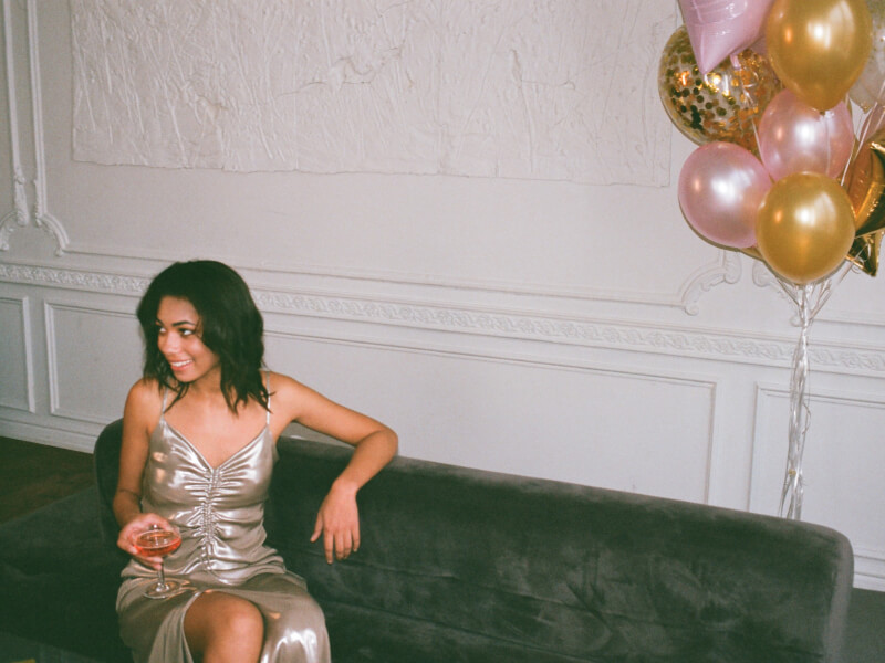 Woman sits on a velvet couch enjoying a drink at her virtual birthday party.