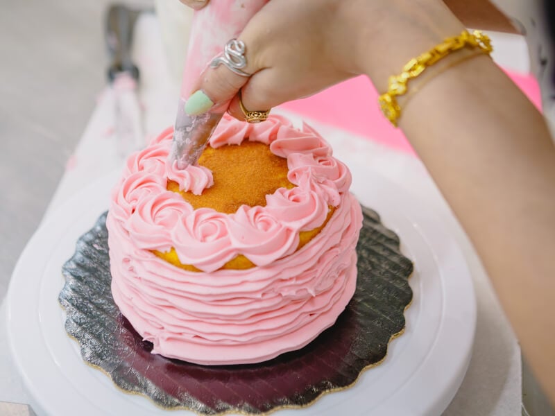 Hands with a piping bag decorating a cake in a cake decorating class