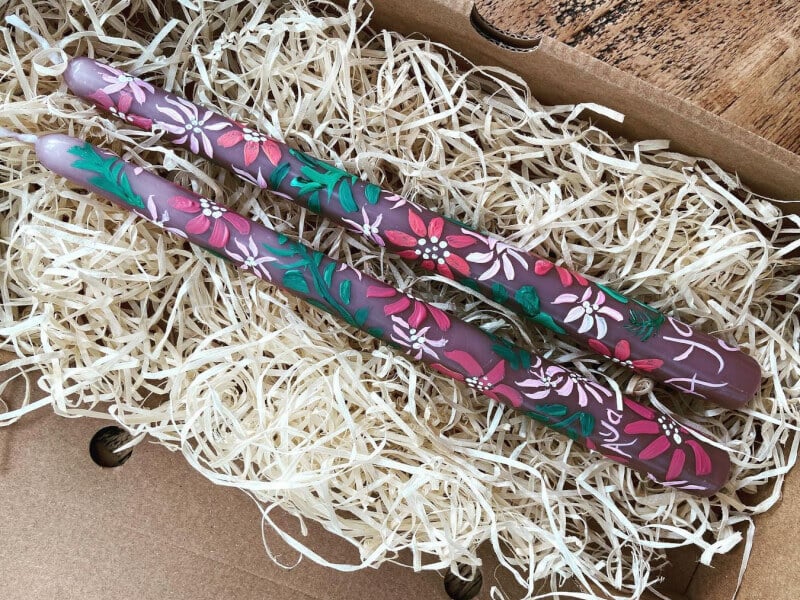 Two painted candles lying on a bed of shredded paper.