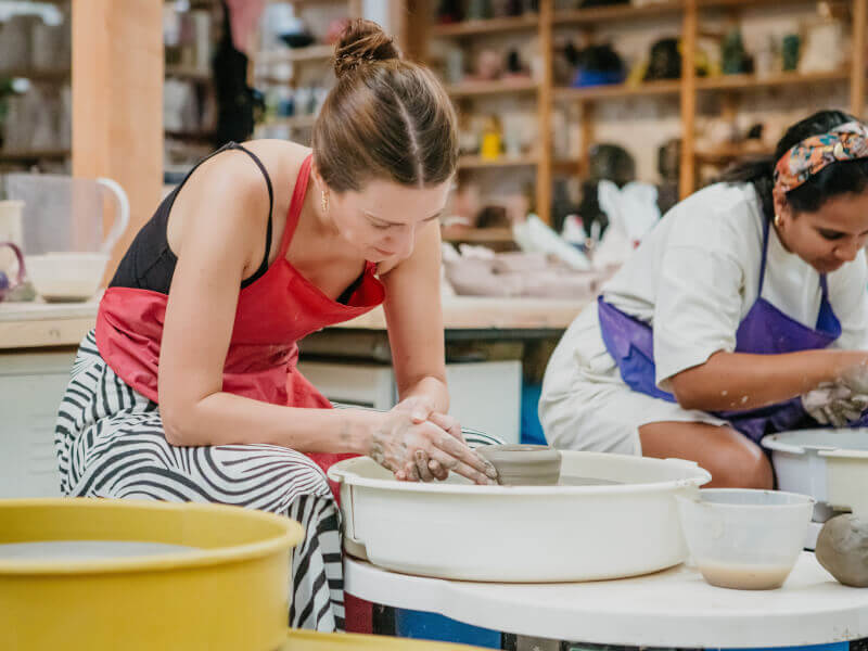A woman makes a pot on the pottery wheel.