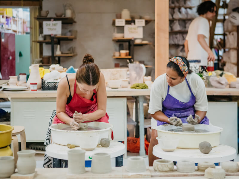 Two women moulding clay on the pottery wheel.