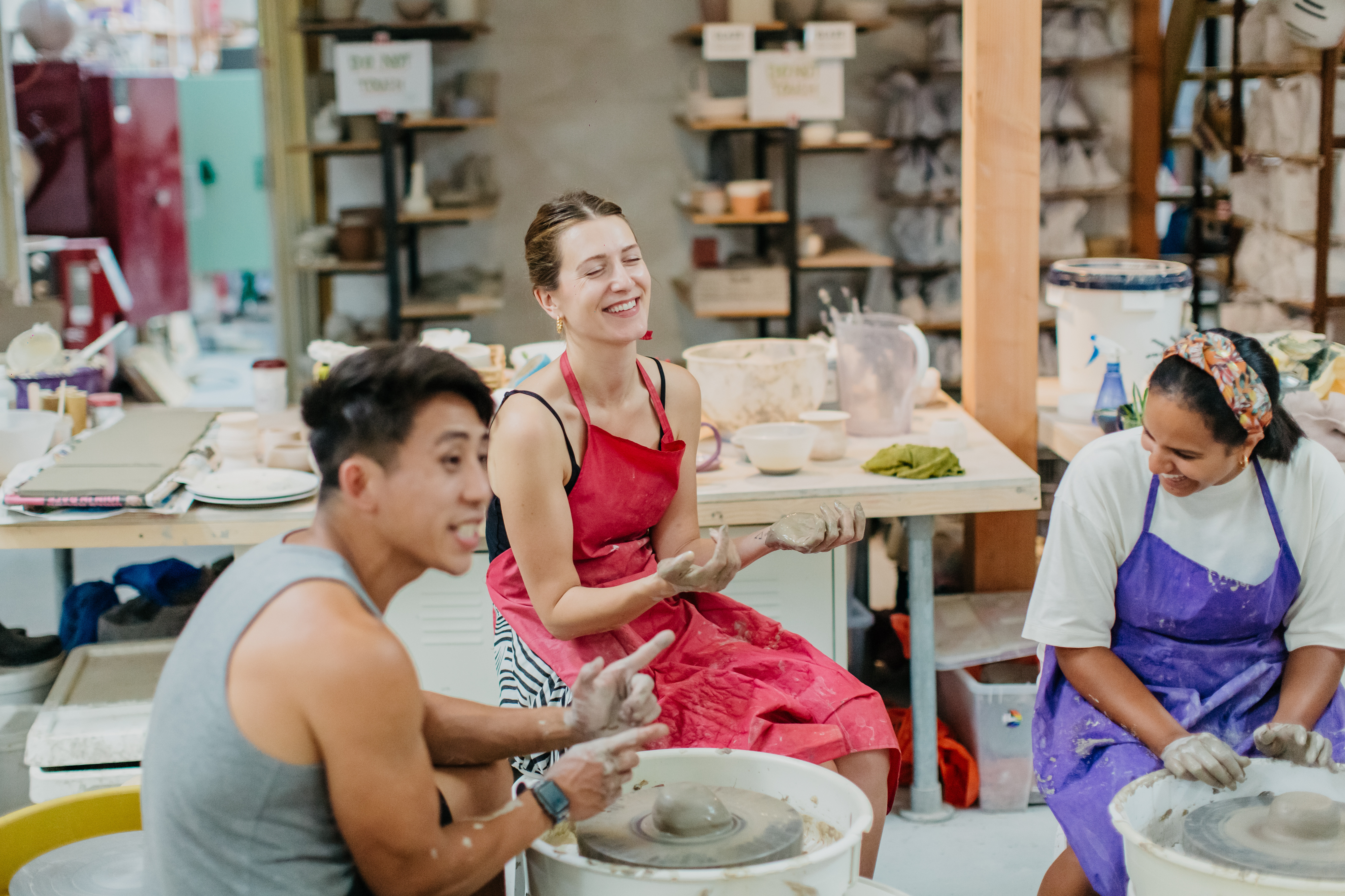 Three people making pottery at a wheel throwing class