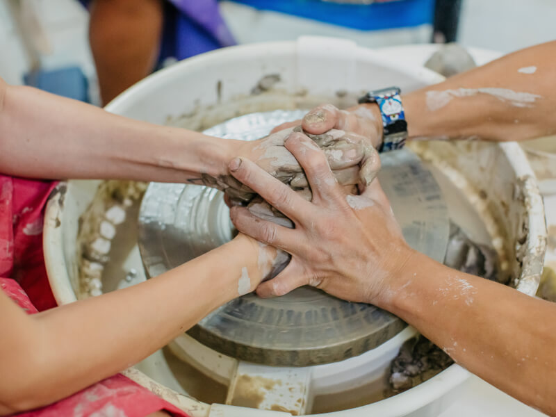 Two hands work clay while wheel throwing at a pottery class.