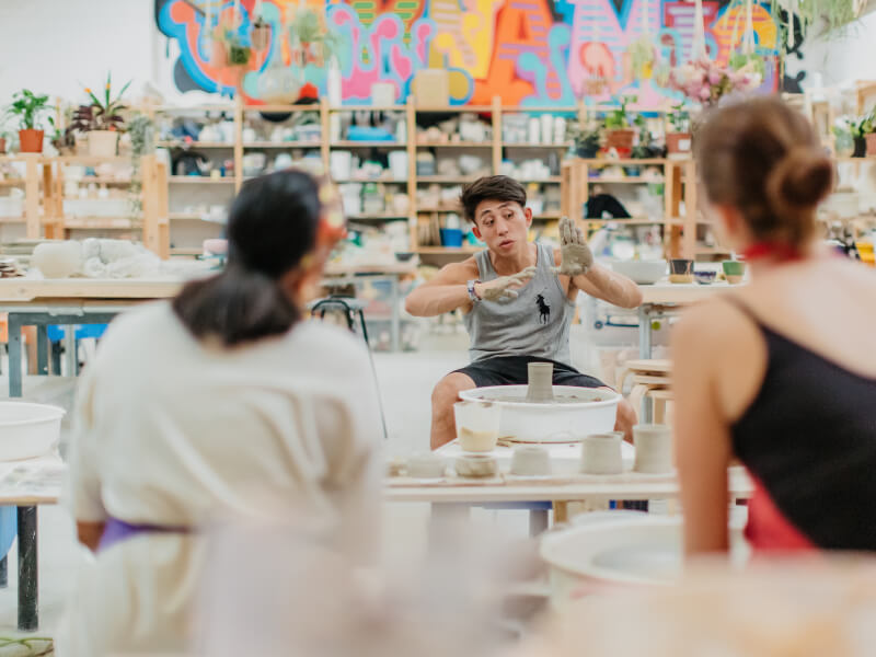 A teacher talking to two students at a pottery class