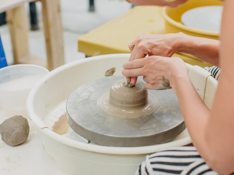 A person uses their hand to sculpt clay on a pottery wheel.