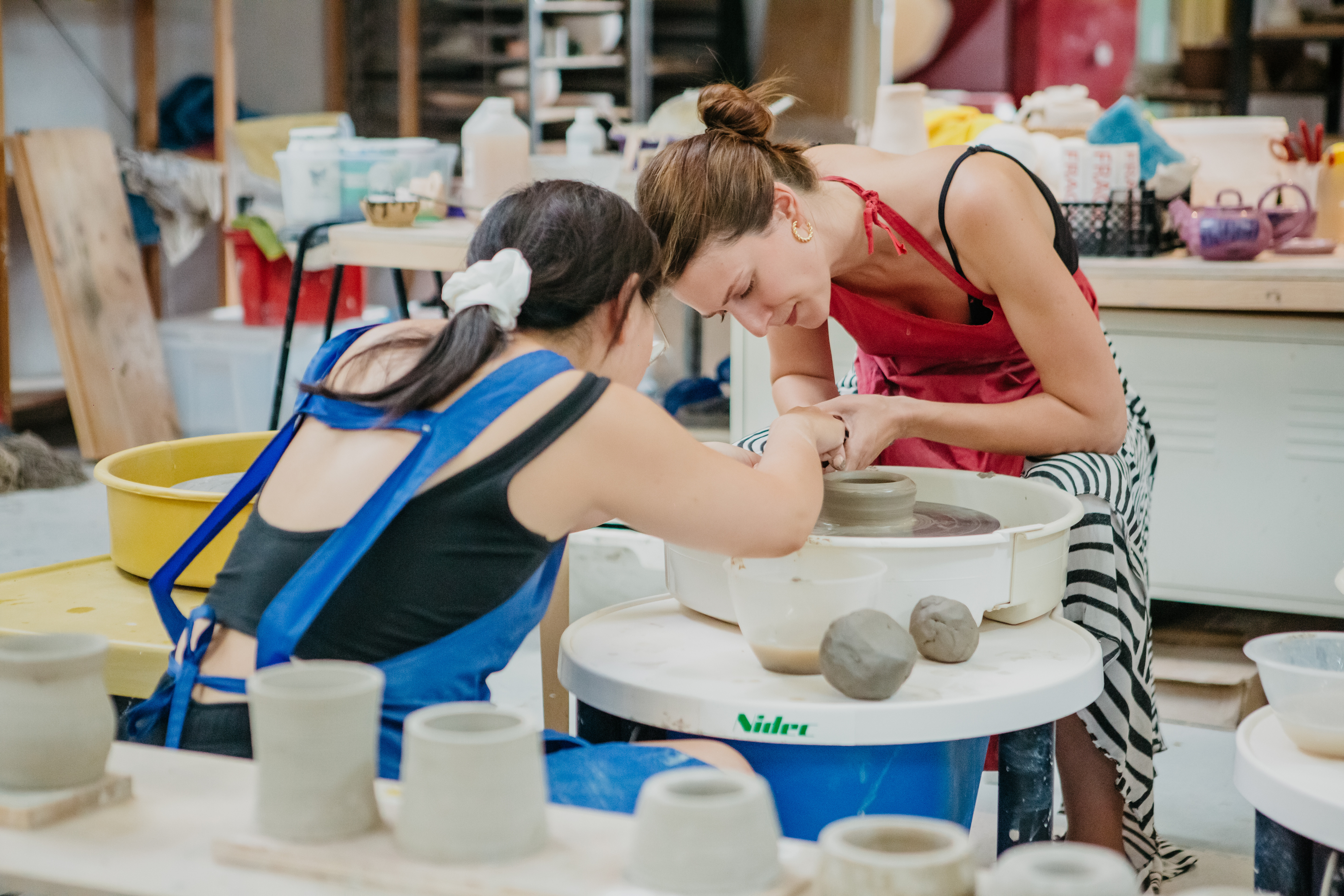 Two women helping each other at a pottery class