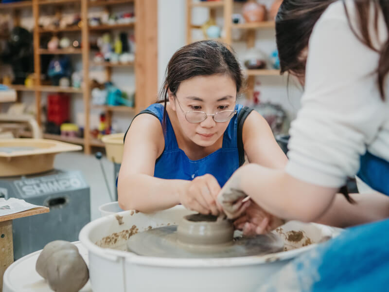 Woman helping someone on a pottery wheel.