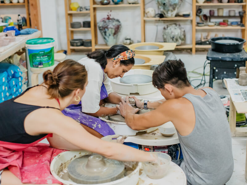 A teacher helping two students at a pottery wheel throwing class. 