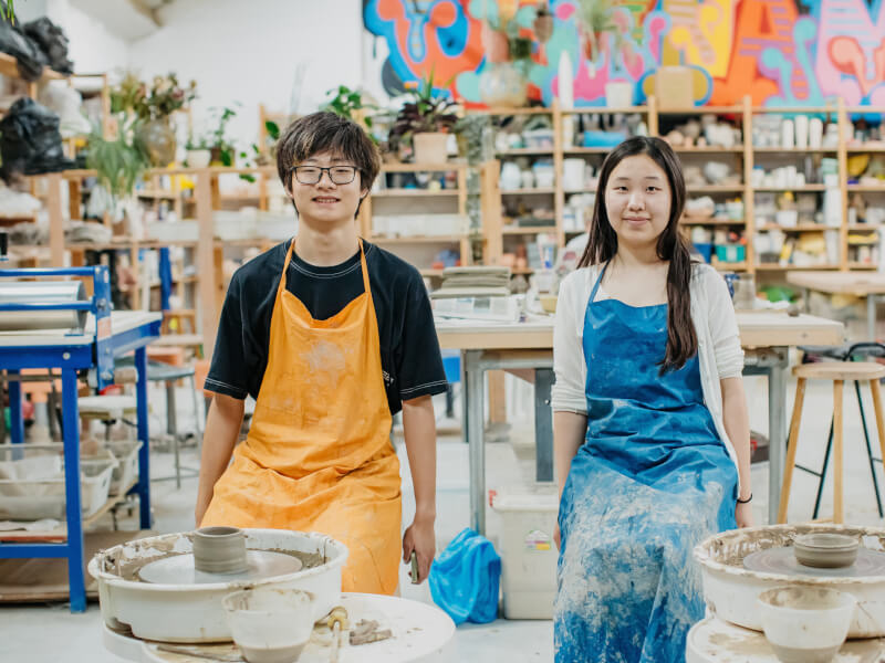 A man and a woman sat behind pottery wheels at a pottery class.