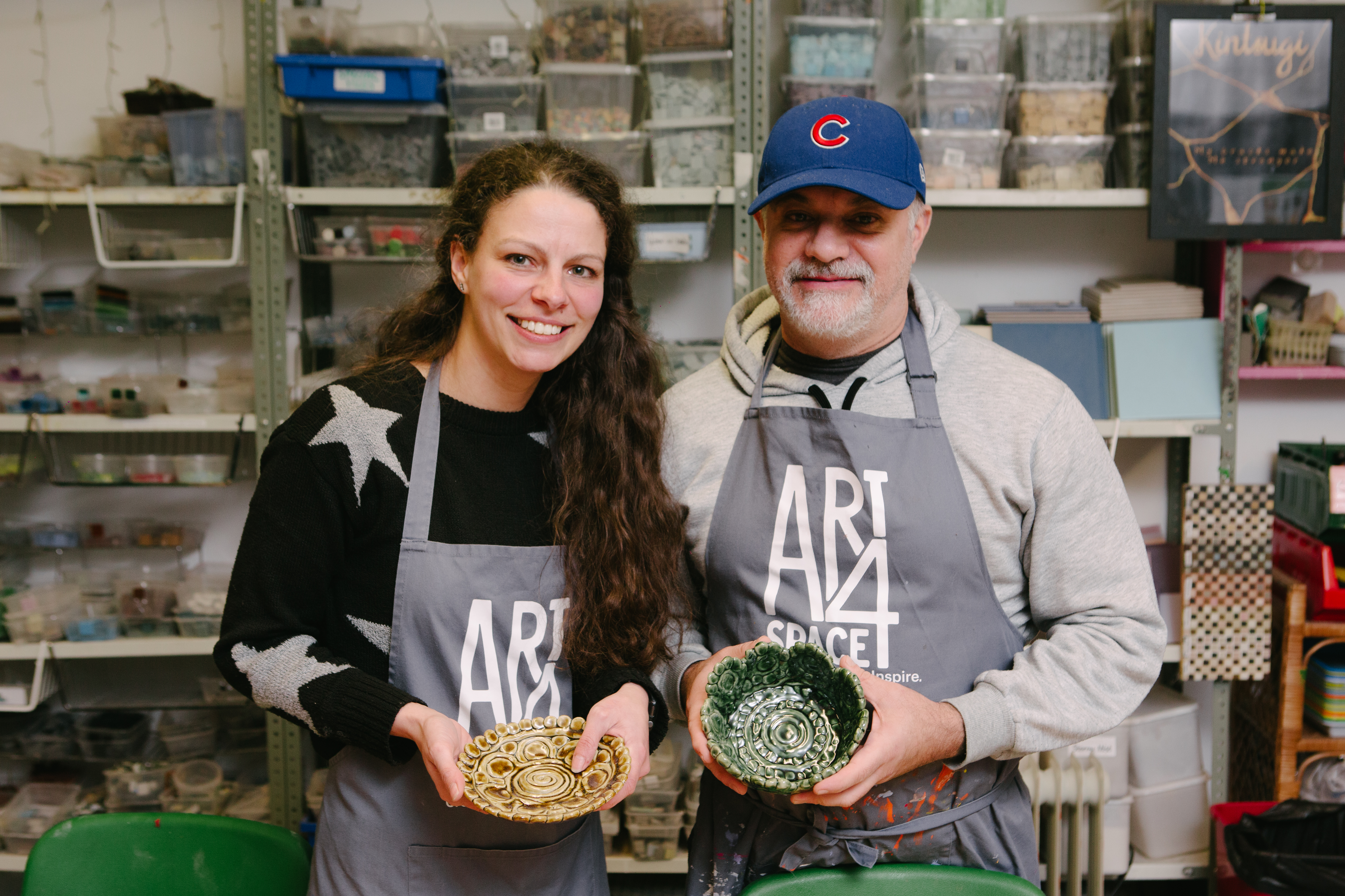 A man and woman are standing up and smiling, holding handmade clay bowls