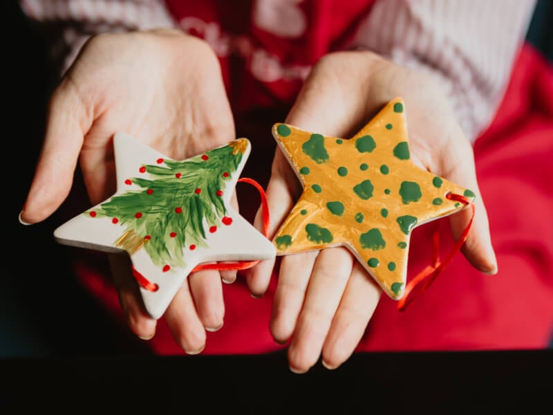 A pair of hands holding star shaped Christmas decorations, painted with festive designs