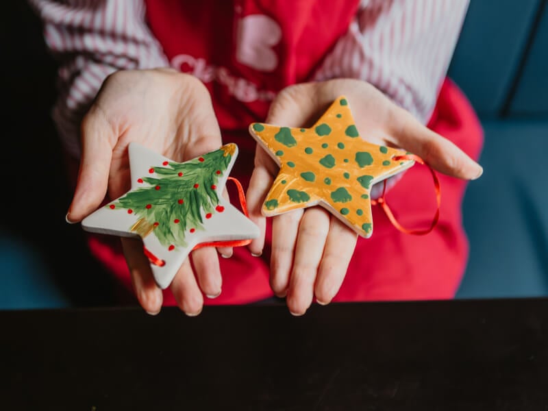 A close up of two hands holding two hand painted Christmas stars